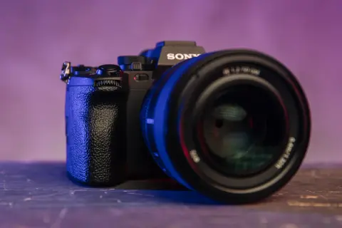 Czarna lustrzanka z kamerą Sony, z obiektywem na pierwszym planie, oświetlona niebieskim i fioletowym światłem.