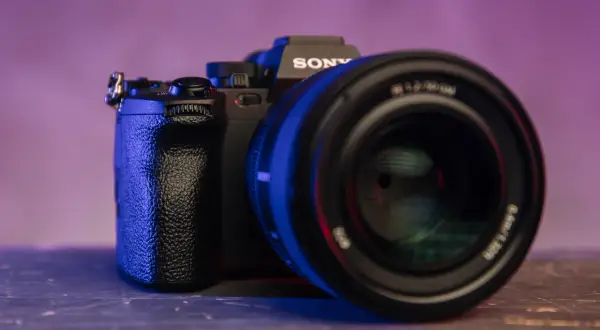 Czarna lustrzanka z kamerą Sony, z obiektywem na pierwszym planie, oświetlona niebieskim i fioletowym światłem.