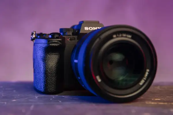 Czarna lustrzanka z kamerą Sony, z obiektywem na pierwszym planie, oświetlona niebieskim i fioletowym światłem.